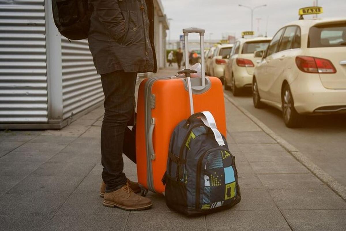 eine Person, die mit einem Koffer und einem Rucksack auf einem Bürgersteig steht