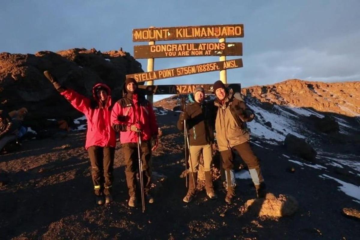 Un grupo de personas de pie junto a un cartel en una montaña.