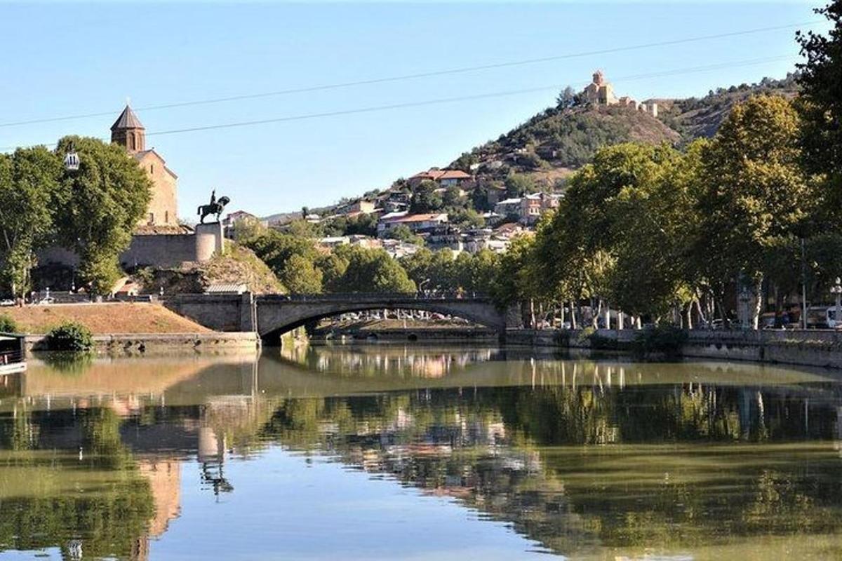 uma ponte sobre um rio com árvores e uma colina