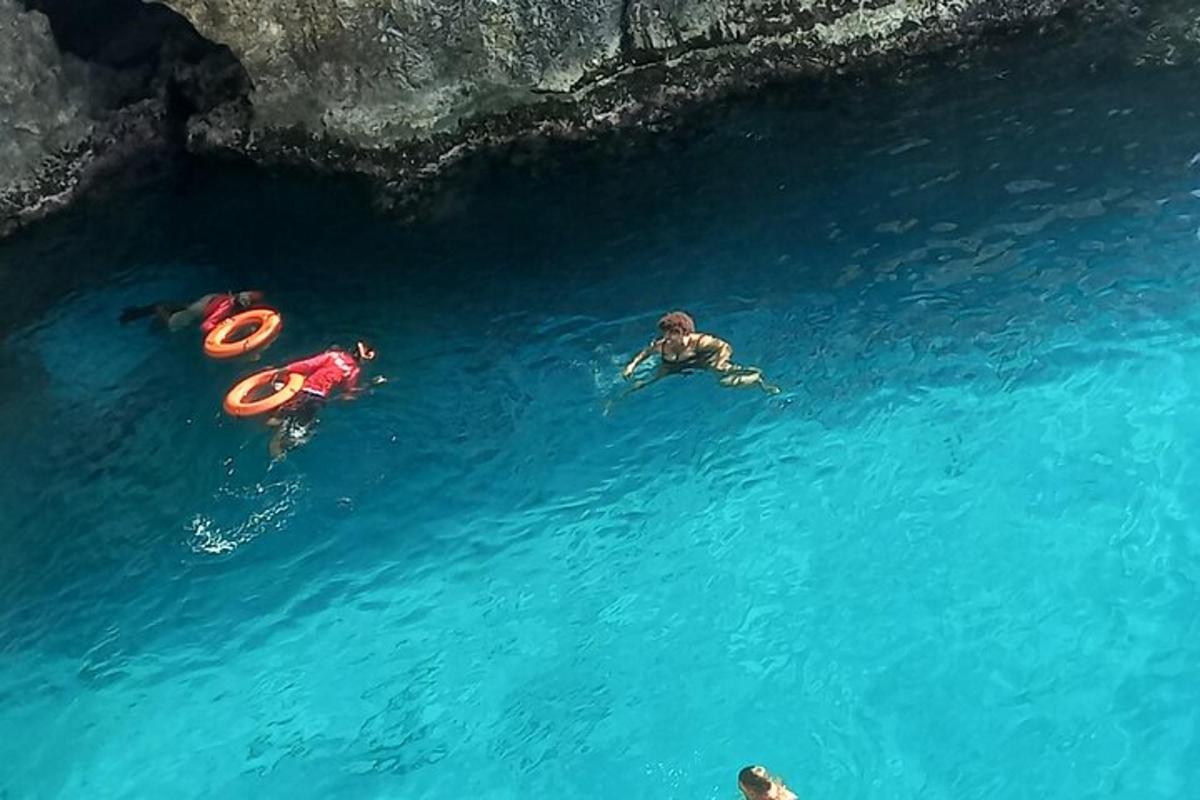 Tres personas nadando en el agua cerca de una cueva.