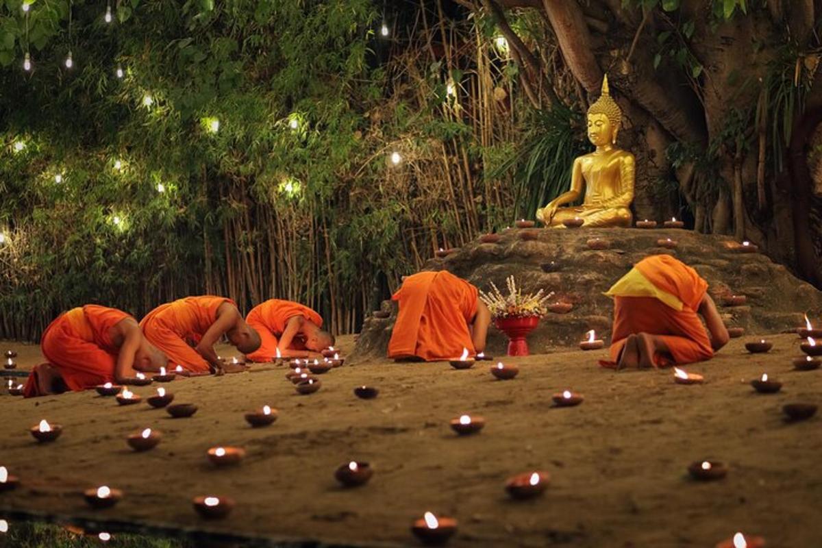 Skupina mnichů zapalujících svíčky před buddhistickým chrámem