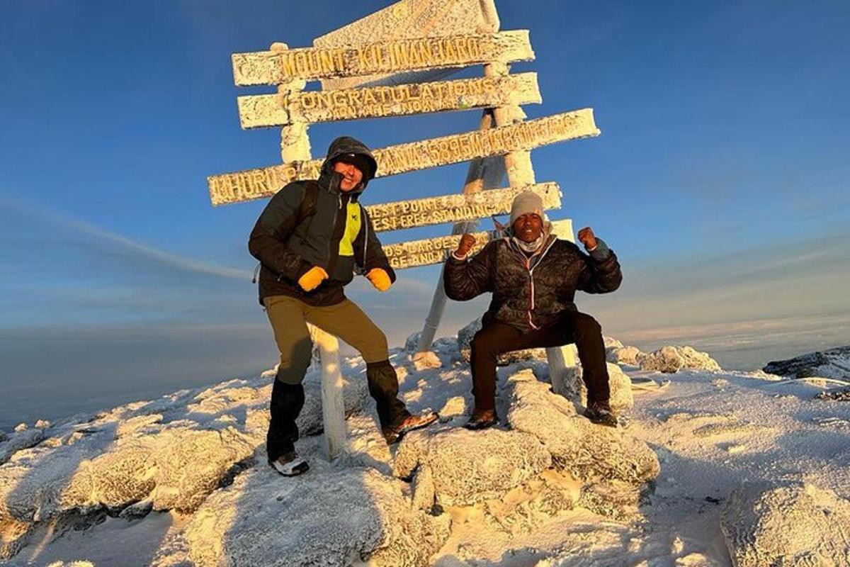 duas pessoas em pé ao lado de uma placa no topo de uma montanha