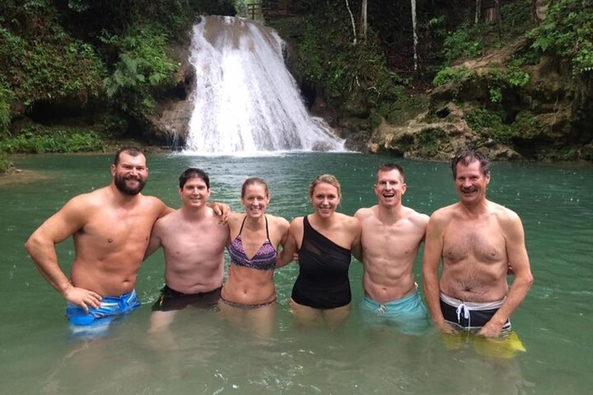 um grupo de pessoas em pé na água em frente a uma cachoeira