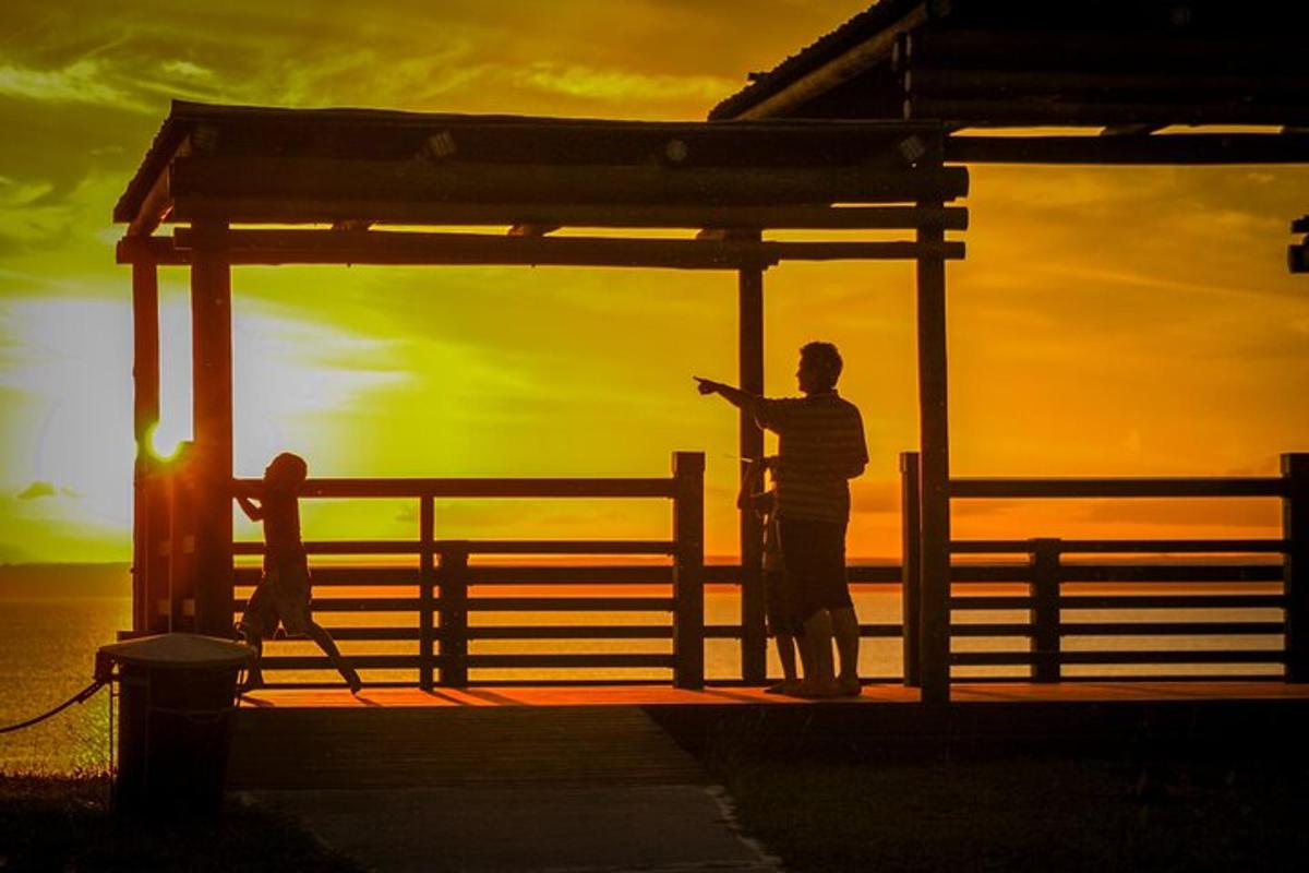 Un hombre de pie junto a una valla con la puesta de sol de fondo.