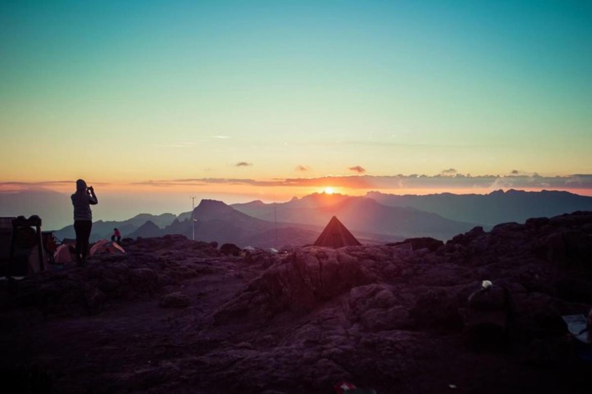 una persona in piedi sulla cima di una montagna che guarda il tramonto