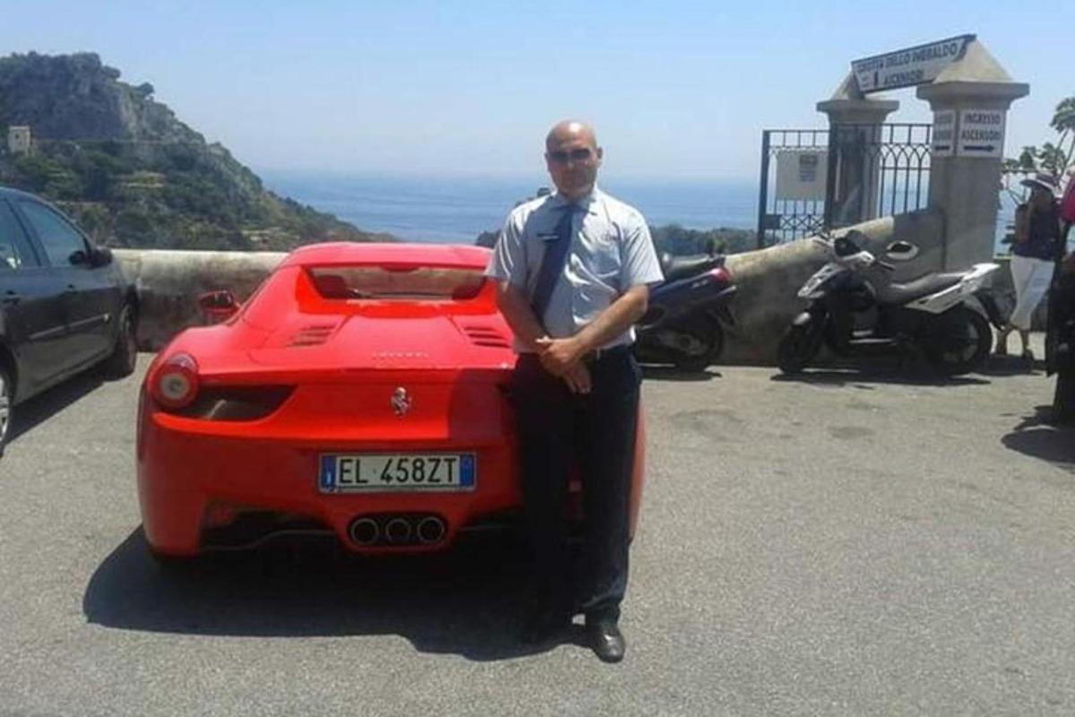 Un hombre está parado junto a un coche rojo.