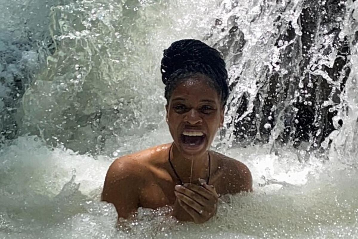 a woman in the water in front of a waterfall