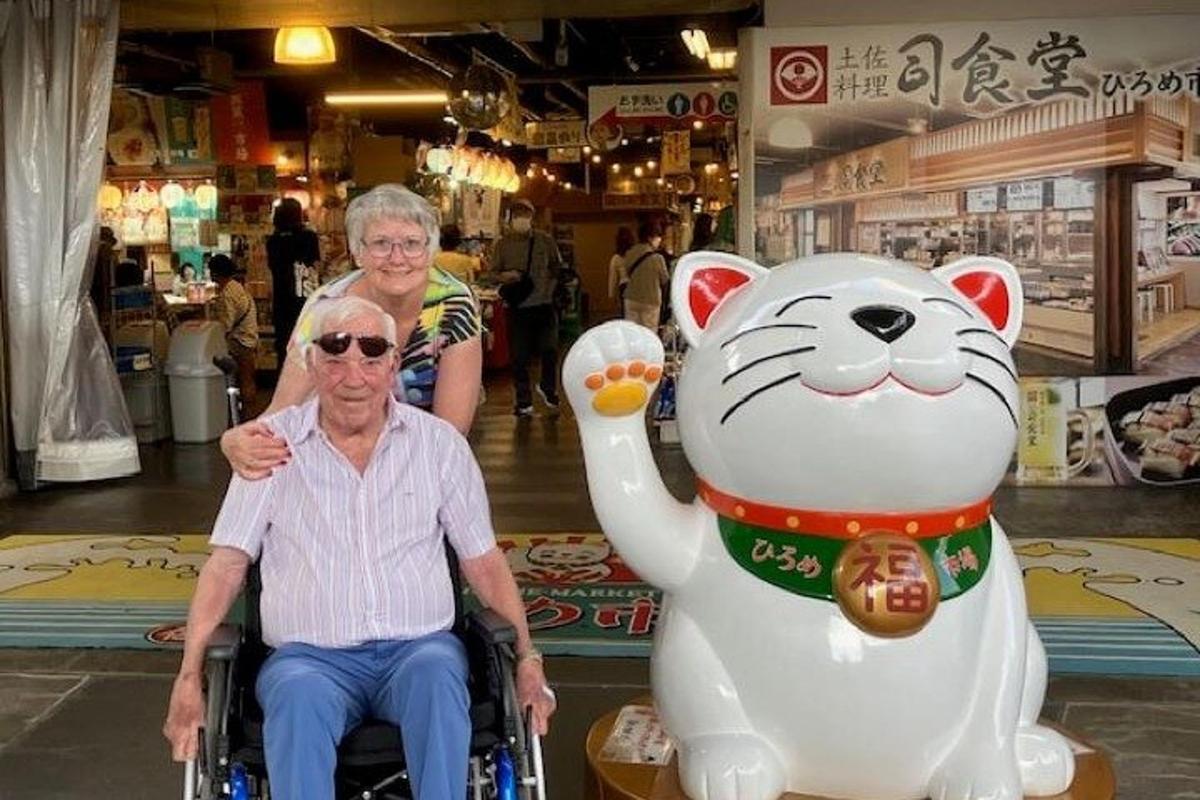 一位坐在轮椅上的老人，旁边是一只巨大的毛绒猫