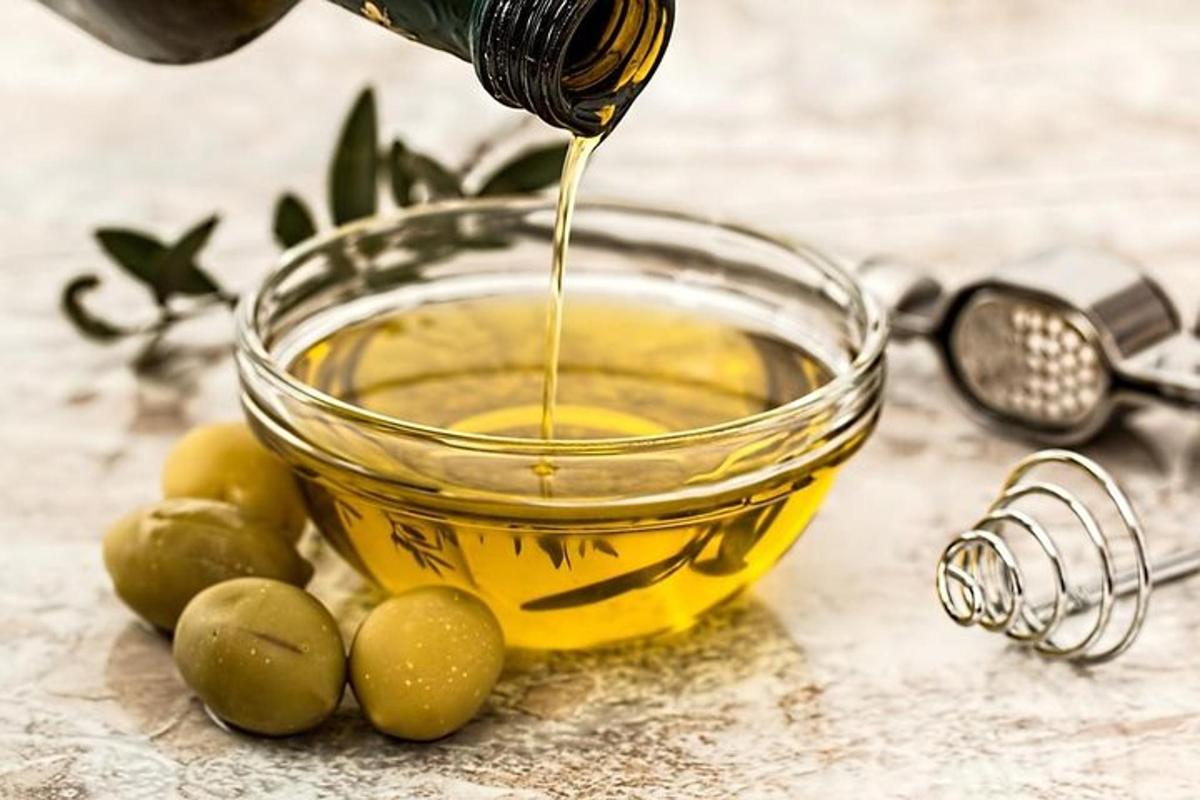 Un recipiente de vidrio lleno de aceite de oliva junto a aceitunas verdes.