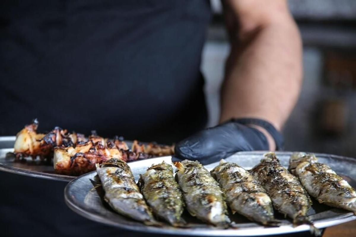 seseorang yang memegang sepinggan ikan bakar dan makanan lain