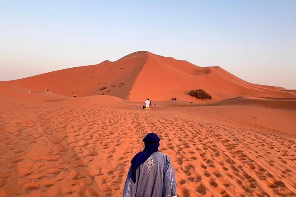 Un hombre caminando por el desierto con un camello en la arena.