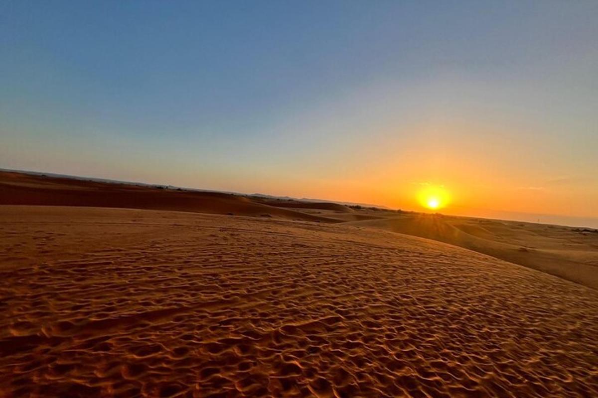 Una puesta de sol en una playa de arena con el sol en la distancia