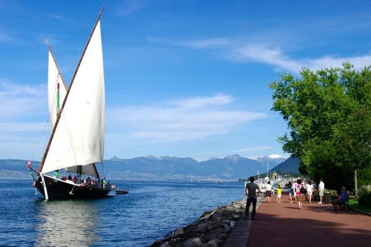 a sail boat in the water with people standing on a dock