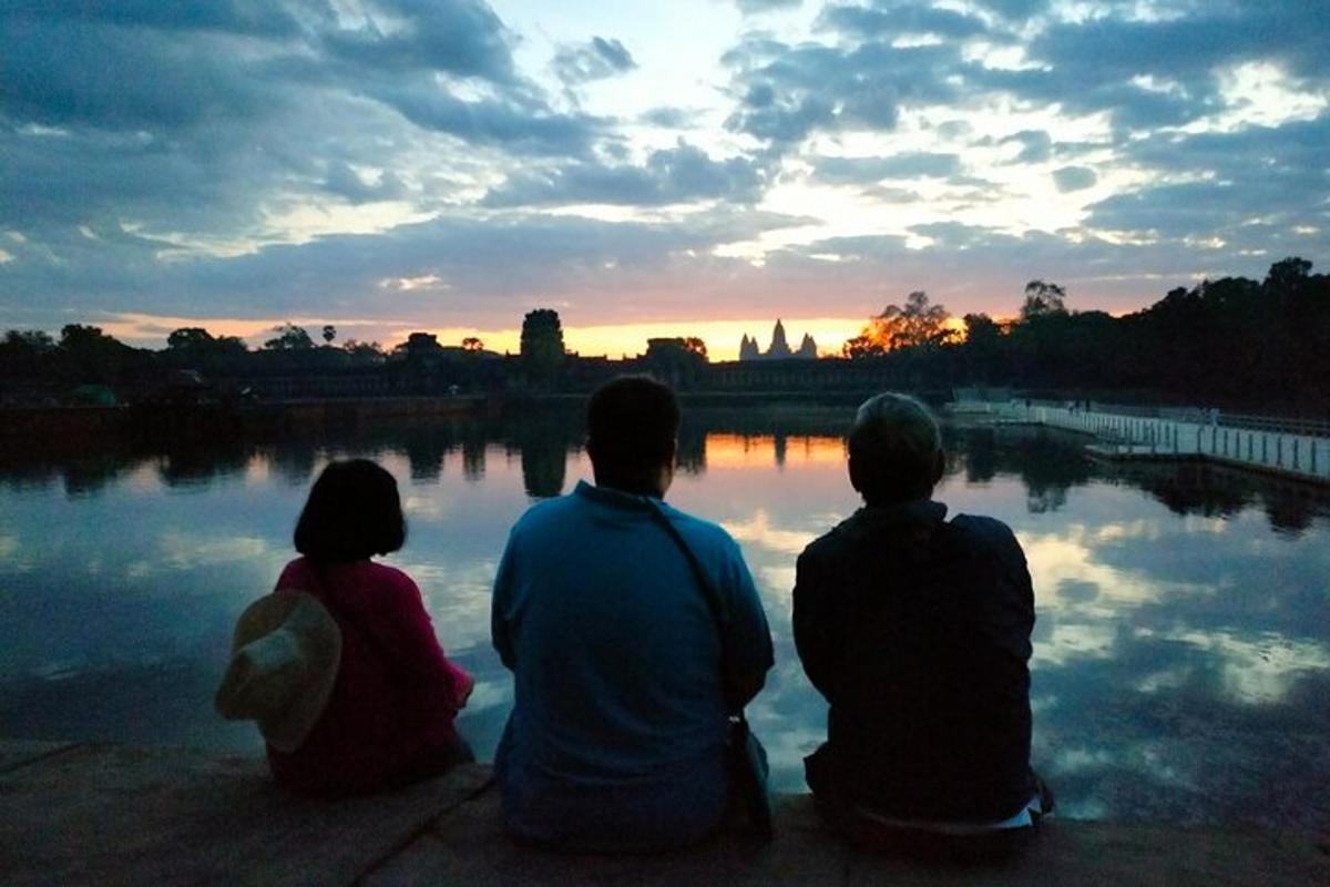tre persone sedute sul bordo di un lago a guardare il tramonto