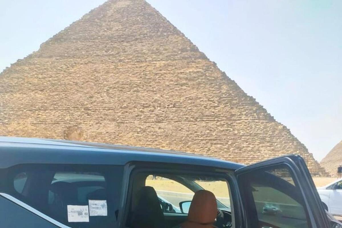 henkilö työntää kätensä ulos autosta pyramidin edessä