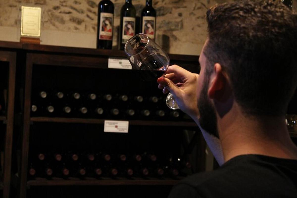 um homem bebendo uma taça de vinho em frente a garrafas de vinho