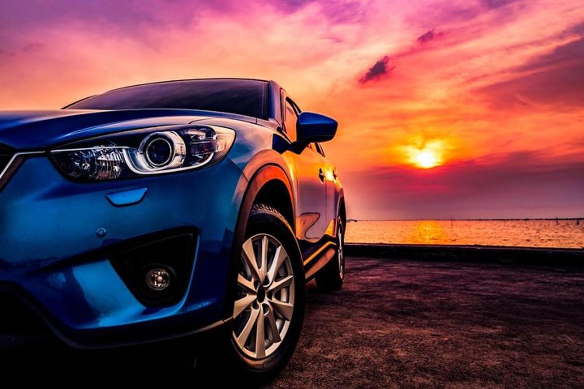 sebuah kereta biru diletakkan di sebelah lautan dengan matahari terbenam