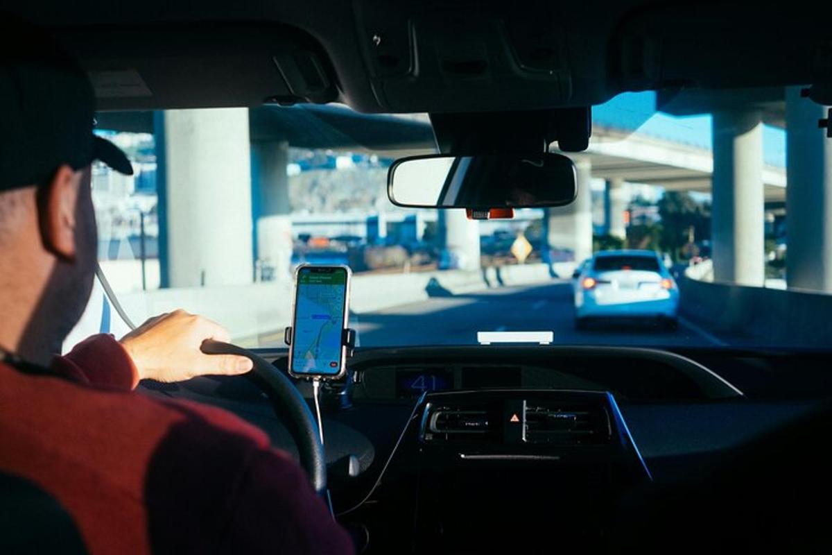 muž řídí auto a dívá se do mobilního telefonu