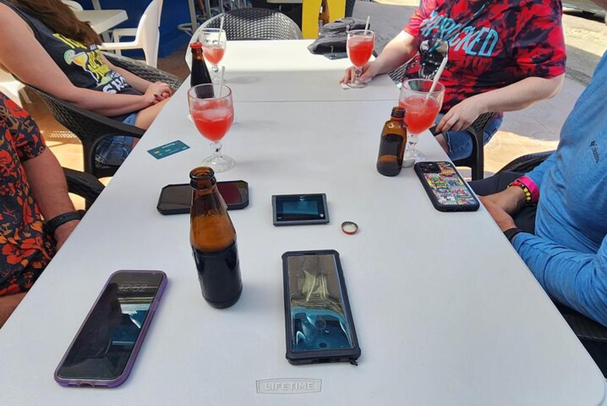 oameni stând în jurul unei mese cu sticle și telefoane mobile