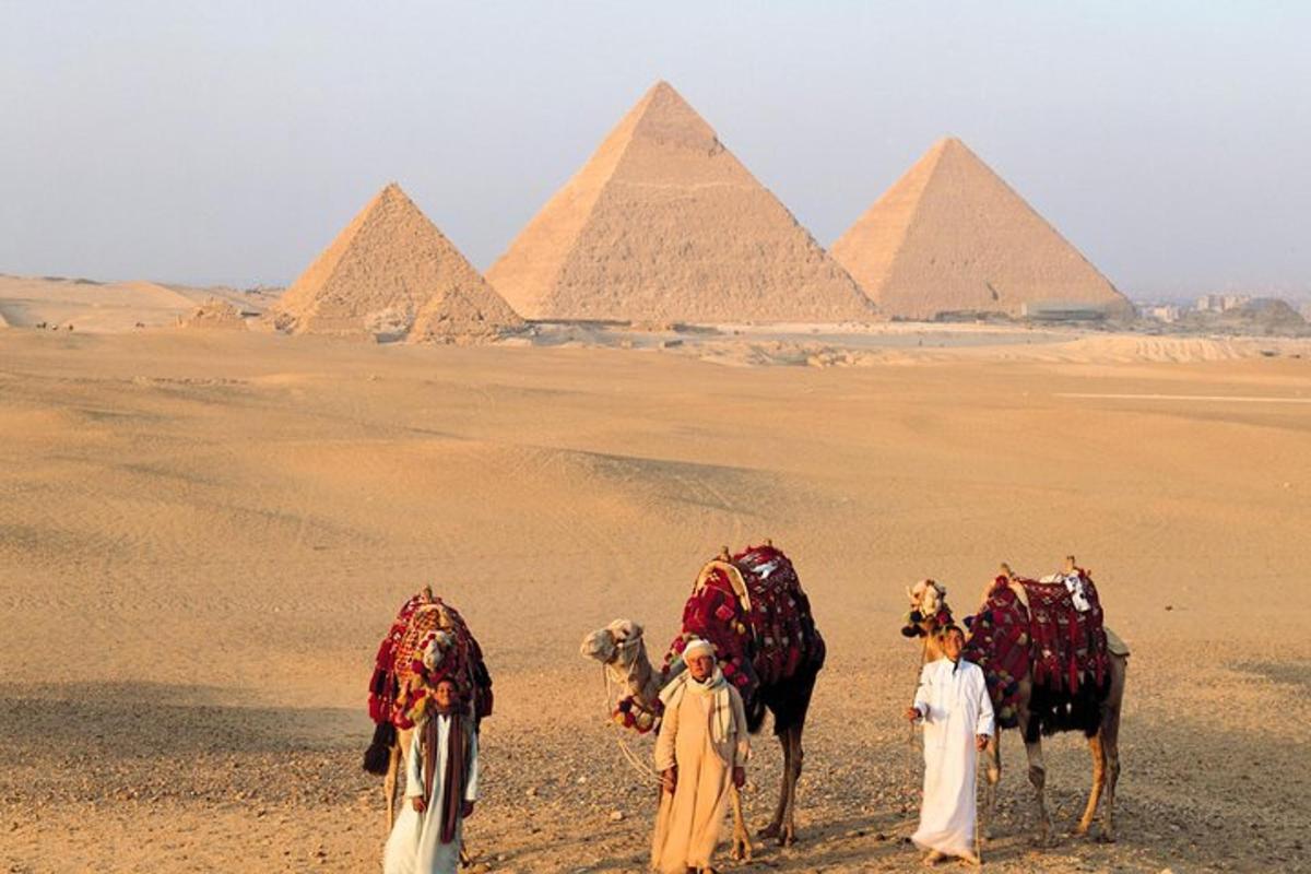 Skupina lidí s velbloudy před pyramidami