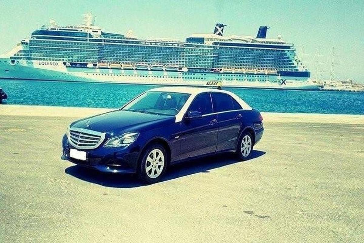 Un coche azul aparcado en la playa con un crucero.