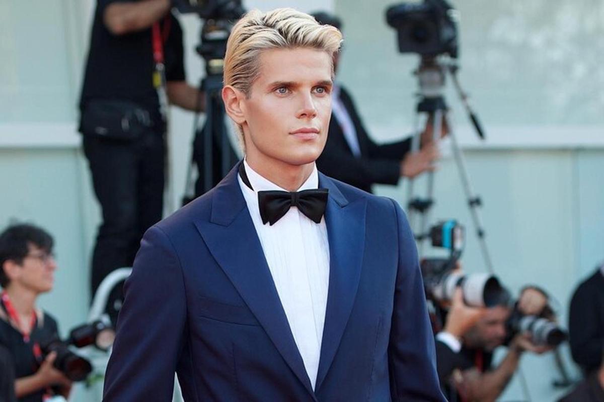 a man in a tuxedo walks the red carpet with a camera