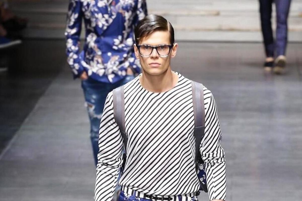 a man wearing glasses walking down a runway