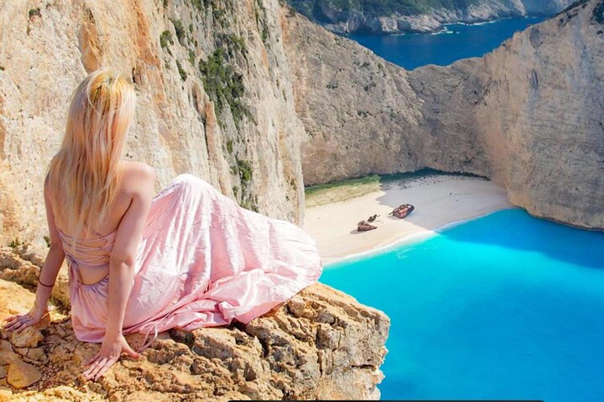 uma mulher de vestido rosa sentada em um penhasco com vista para uma praia