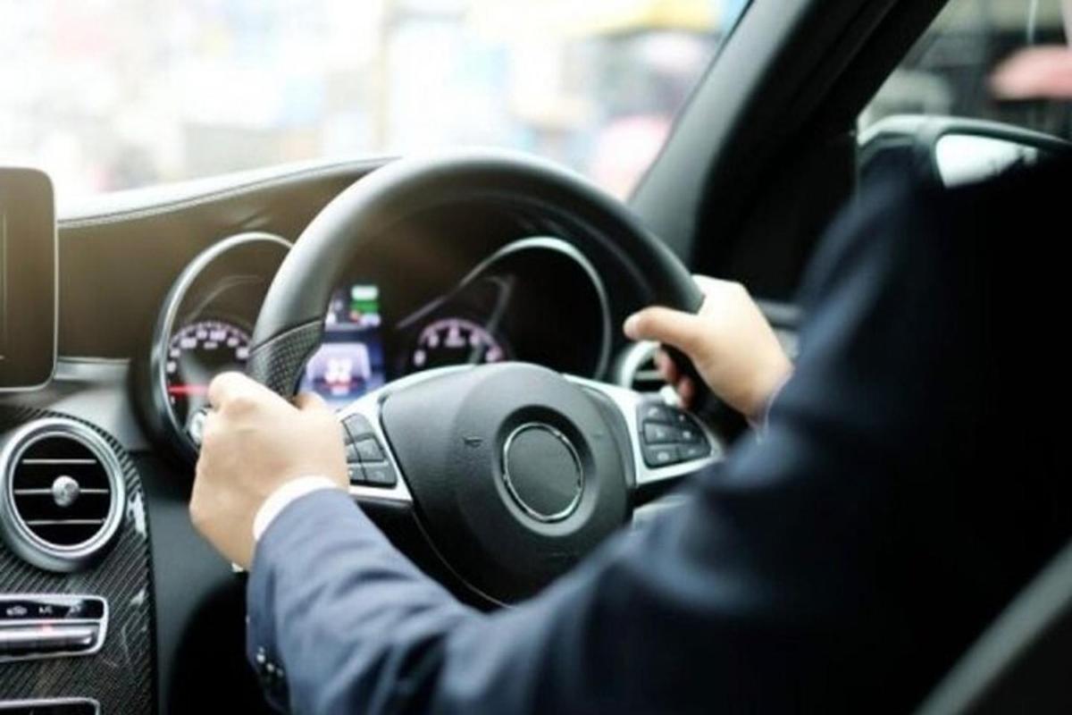 seorang pria mengendarai mobil dengan tangannya di roda kemudi