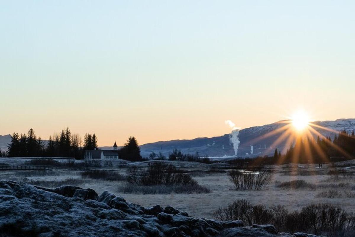 a sunset in a field with the sun shining on a mountain