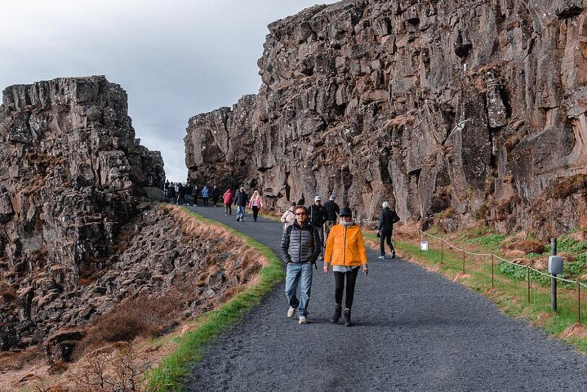 pessoas caminhando por uma estrada ao lado de uma parede de pedra