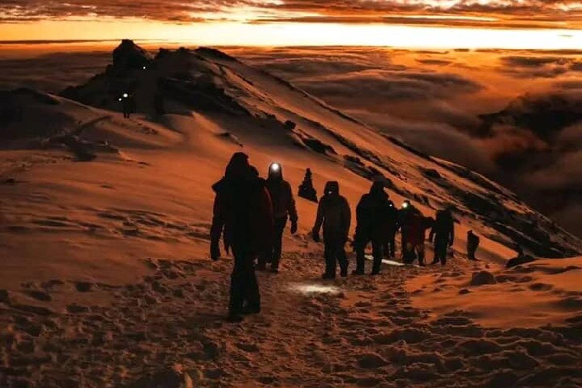 sekumpulan orang berjalan mendaki gunung pada waktu matahari terbenam