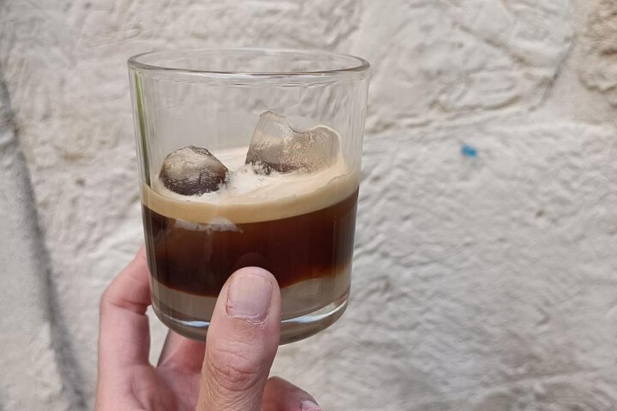 uma mão segurando um copo de café com um biscoito dentro