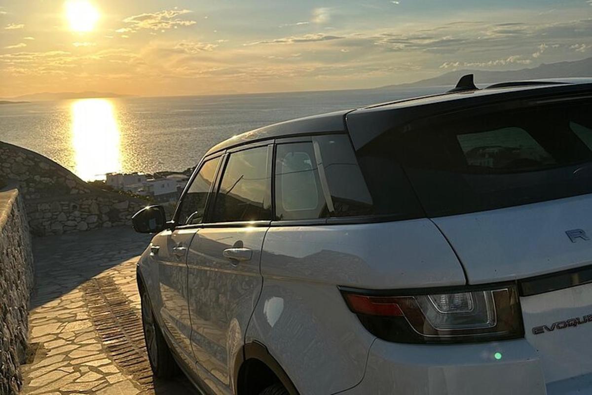 ein weißes Auto, das neben dem Meer mit dem Sonnenuntergang geparkt ist