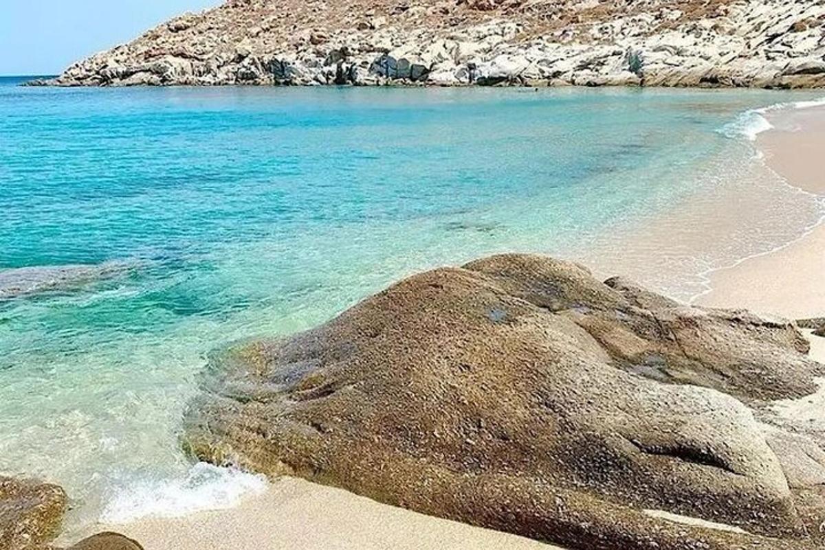 ein Strand mit blauem Wasser und einem großen Felsen