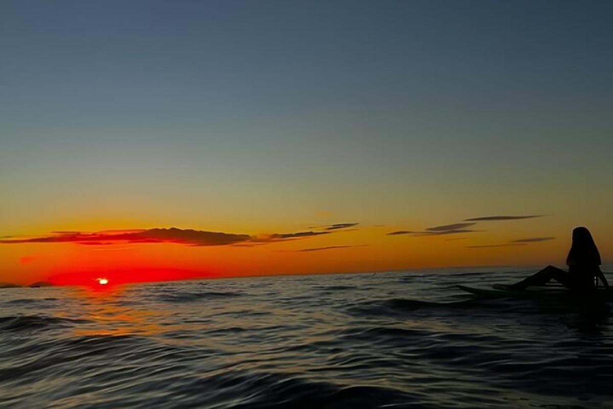 una persona seduta sulla spiaggia a guardare il tramonto