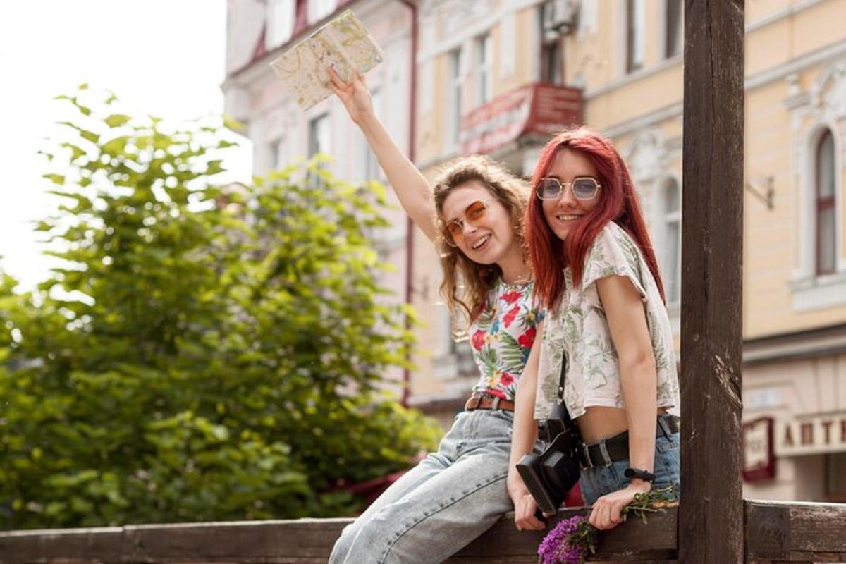Két lány ül egy kerítésen, és egy táblát tart a kezében