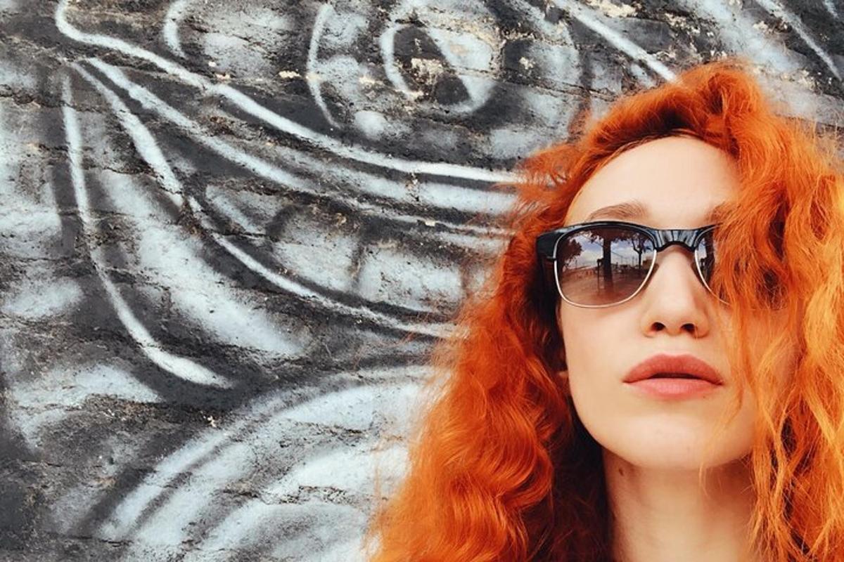жена с червена коса и слънчеви очила пред стена