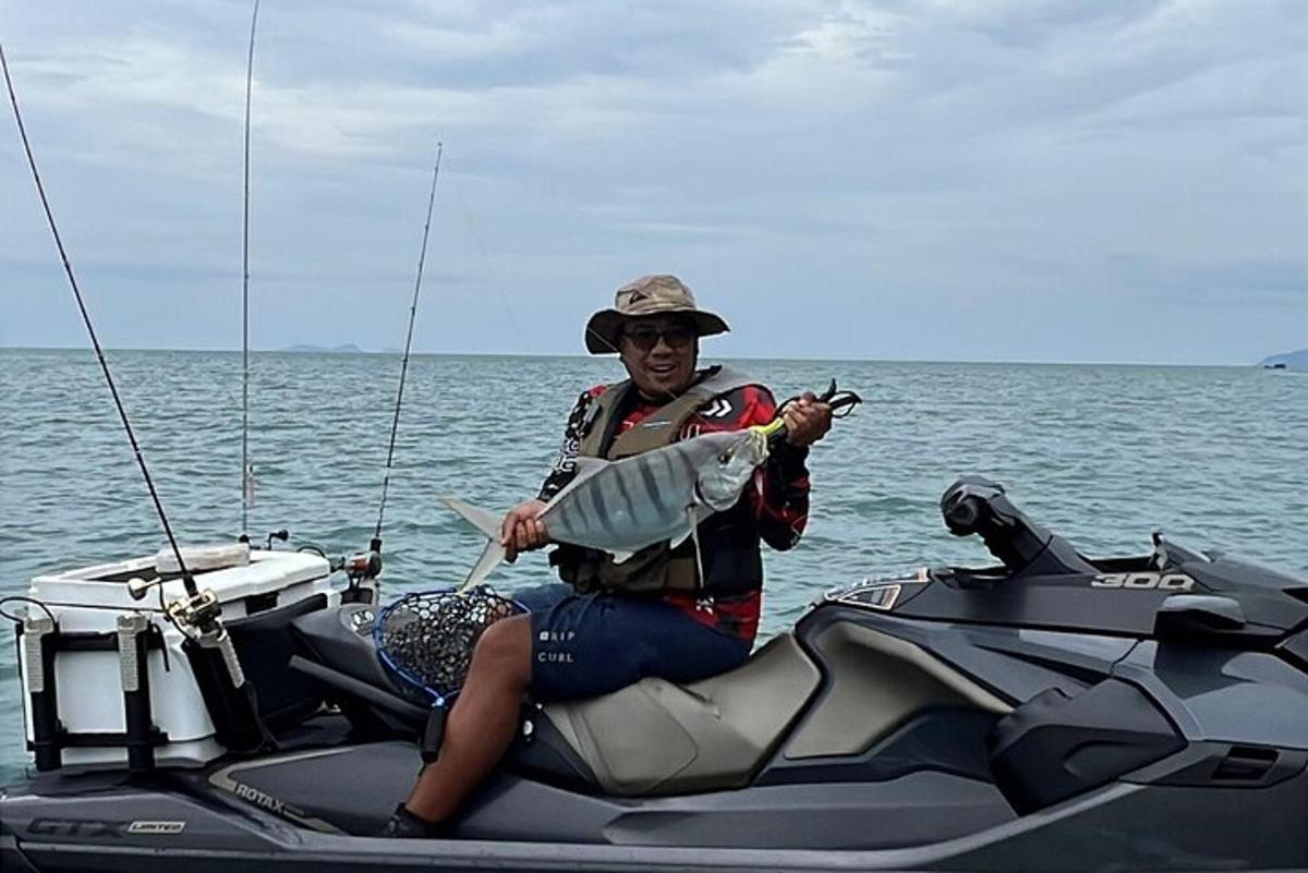seorang lelaki menaiki jet ski memegang ikan di dalam air
