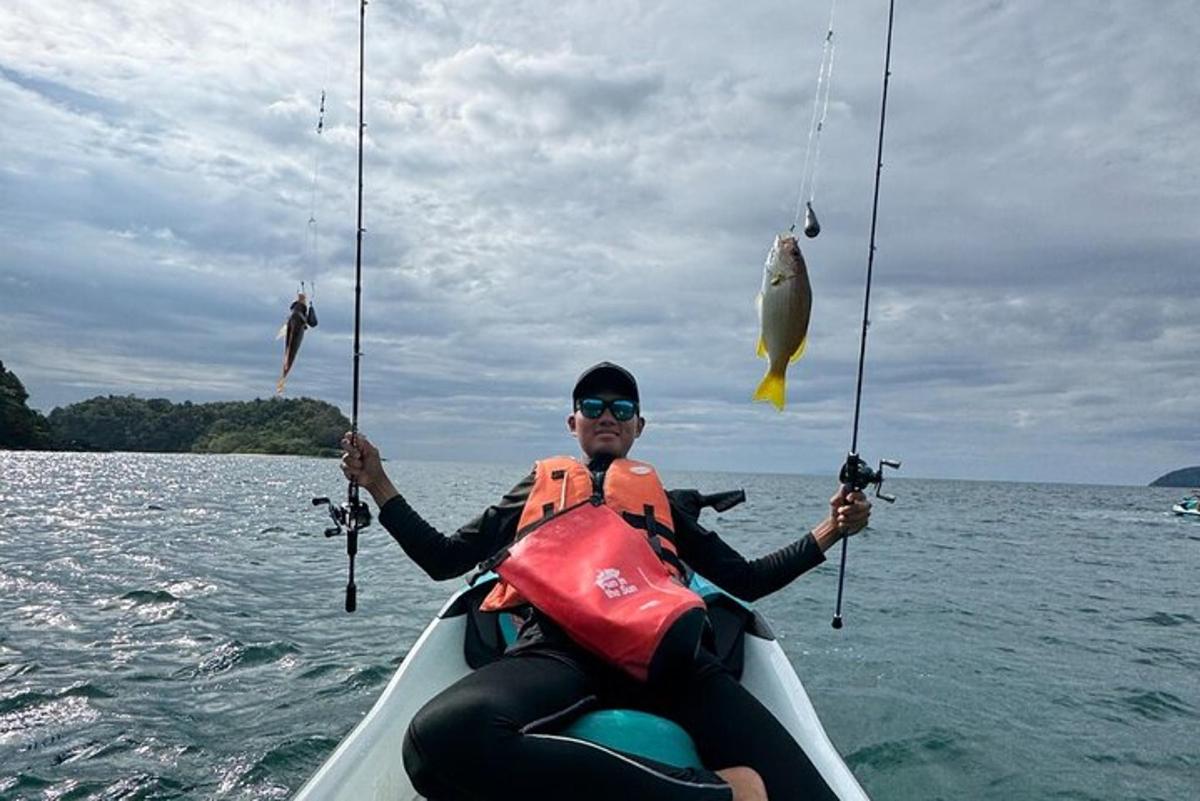 seorang lelaki di dalam bot memegang dua batang pancing dan seekor ikan