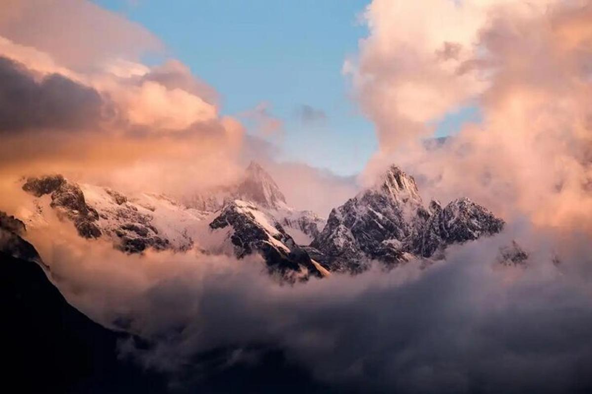 a mountain covered in snow and clouds in the sky