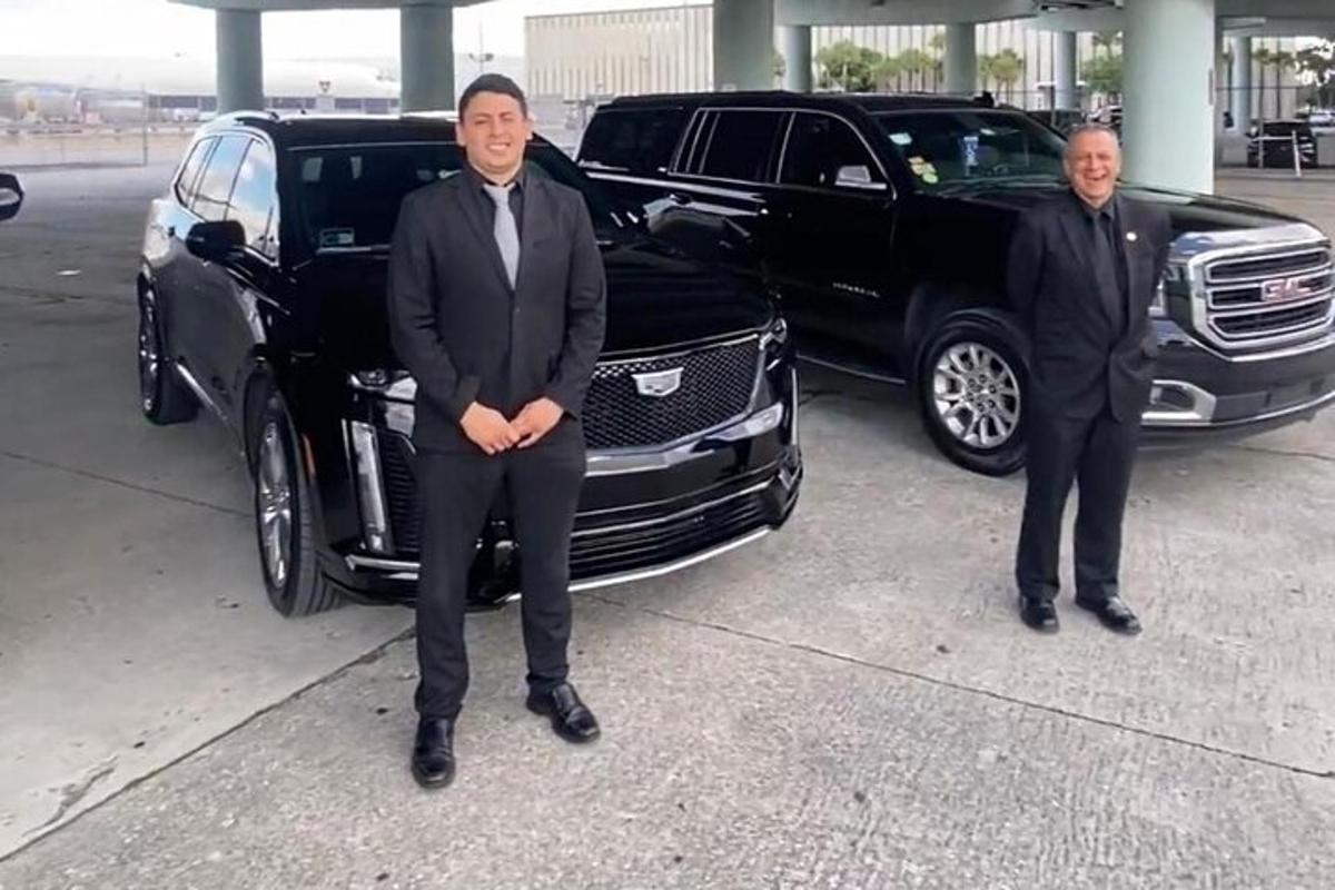 två män i kostymer står bredvid en svart limousine