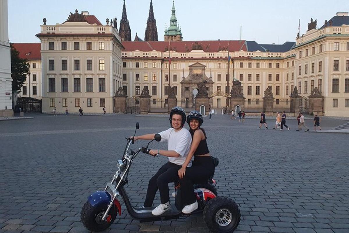 Un hombre y una mujer viajan en scooter frente a un edificio.