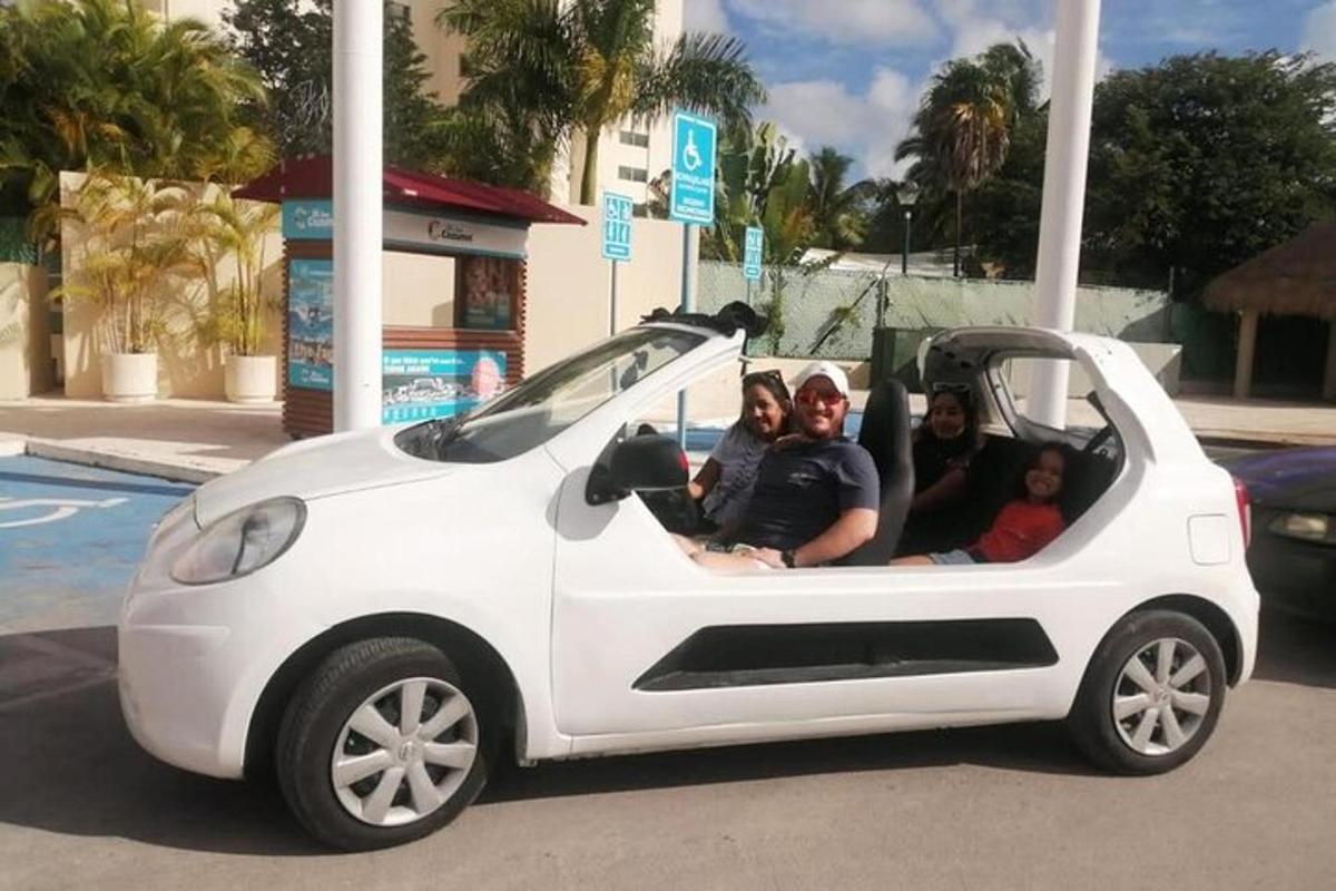grupė žmonių, sėdinčių mažame baltame automobilyje