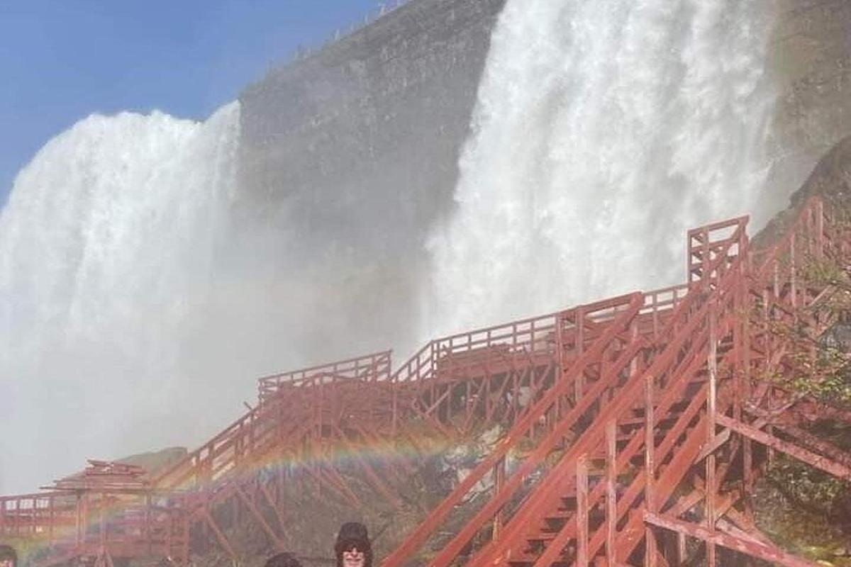 a person standing in front of a waterfall with a rainbow