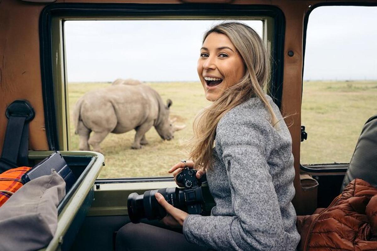 a woman with a camera on a train looking at a rhino