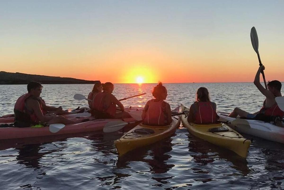 en gruppe mennesker som sitter i kajakker i vannet ved solnedgang
