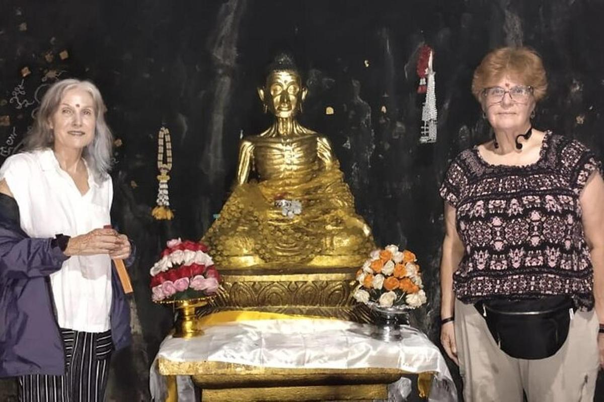 two women standing in front of a golden buddha statue