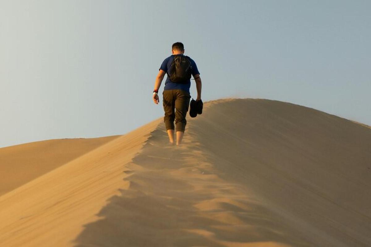 Un hombre caminando por una duna de arena en el desierto