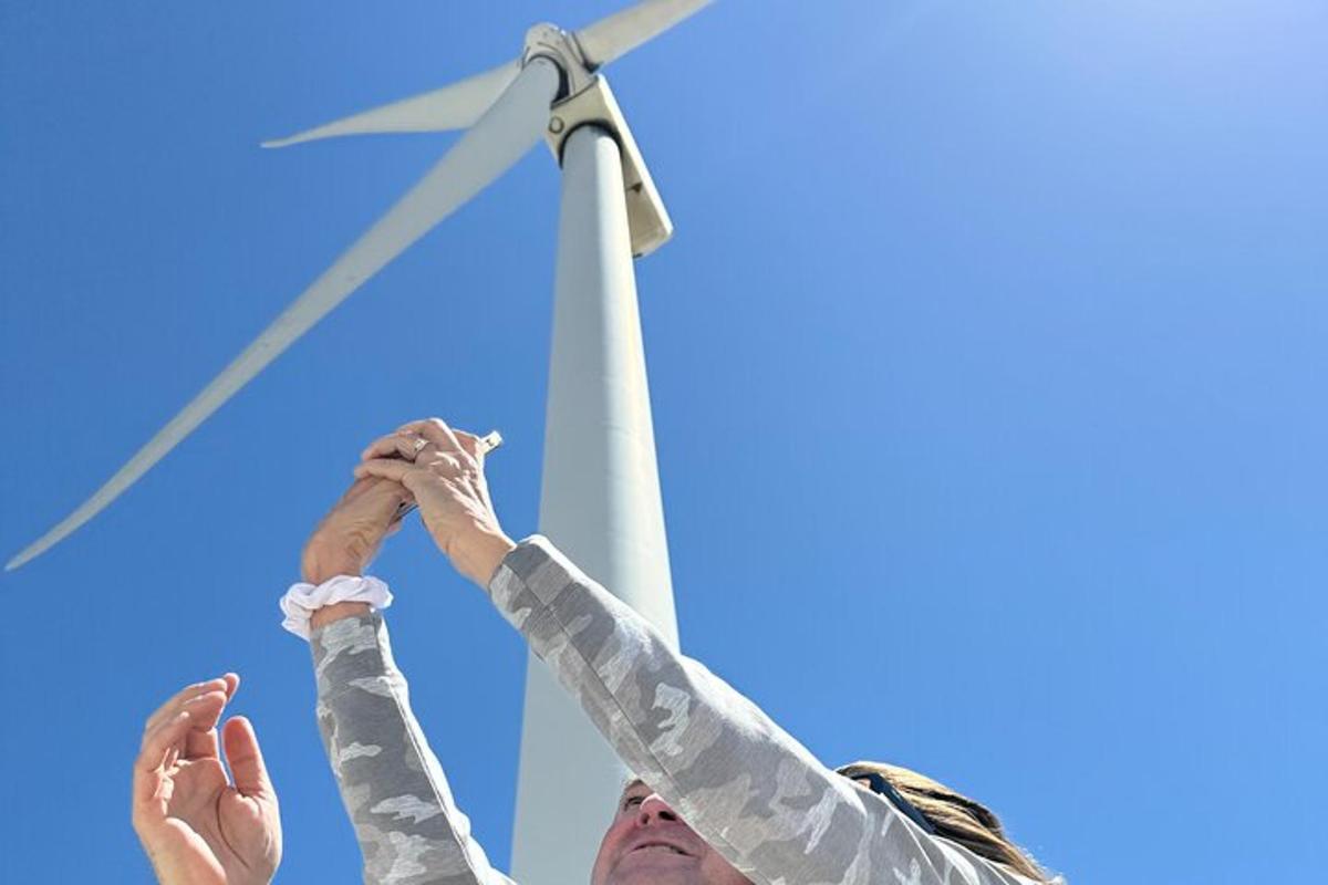a man and woman holding their hands up in front of a wind turbine